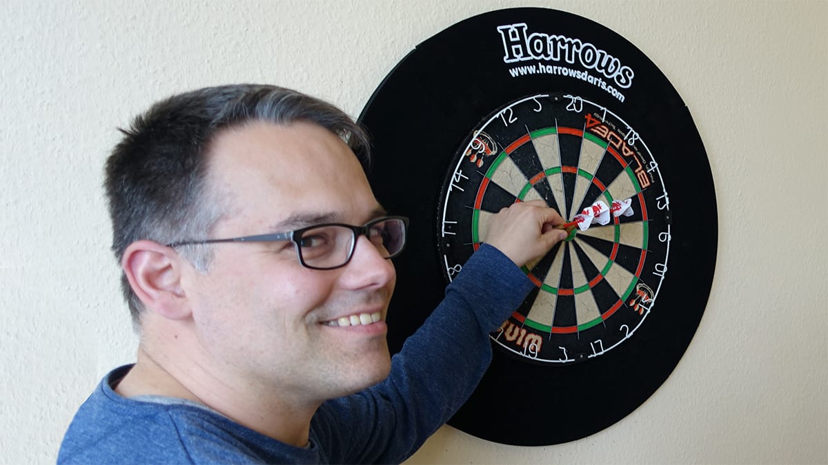 Mann zieht Pfeil aus einer Dartscheibe